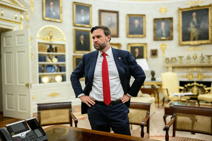 JD Vance standing in a formal office looking frustrated with hands on hips amid historic portraits and elegant decor.