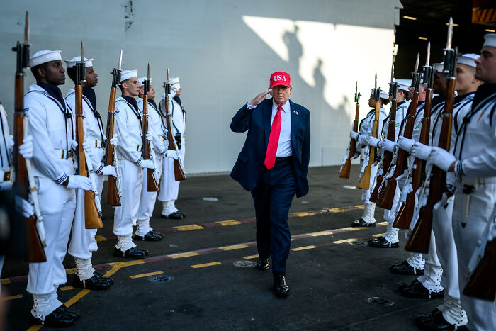 Former President Trump in a red USA hat salutes naval officers amid rising tensions between U.S. and Venezuela.