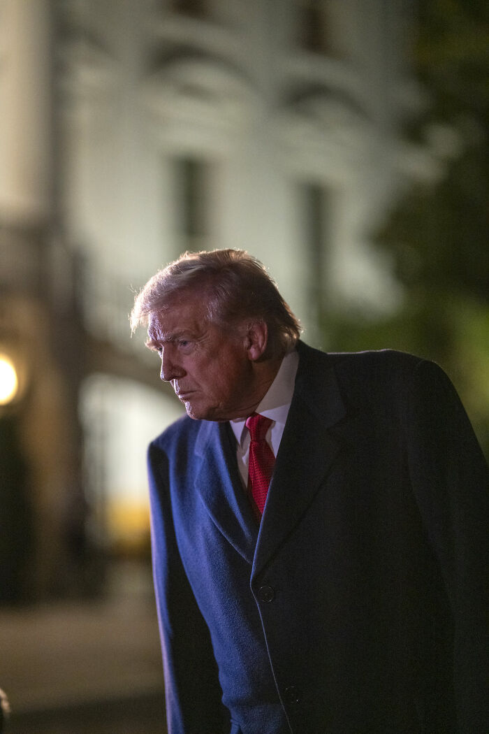 Donald Trump outdoors at night wearing a dark coat and red tie in a candid moment with blurred background.