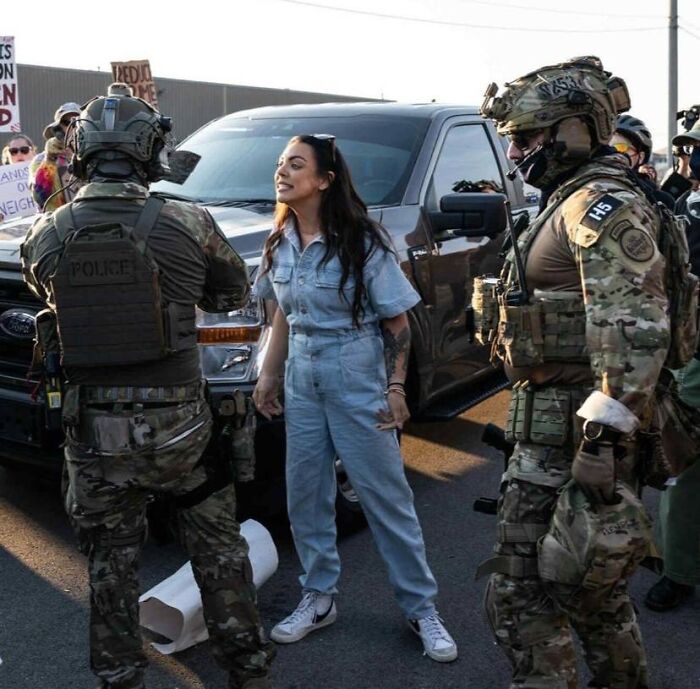 Protester confronts National Guard troops in tactical gear during Chicago deployment dispute amid public demonstration.