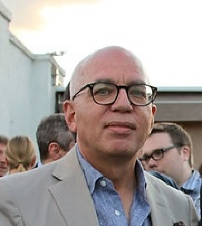 Michael Wolff wearing glasses and a beige jacket at an outdoor event, related to Trump biographer Epstein lawsuit news.