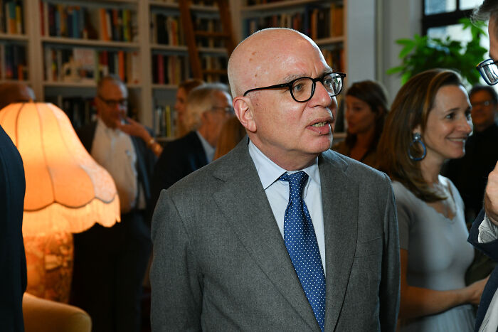 Michael Wolff in a gray suit and blue tie at a social event, related to Trump biographer lawsuit and Epstein case.