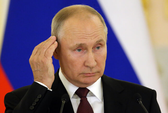 Vladimir Putin speaking at a podium with Russian flag colors in the background, relating to Putin&rsquo;s war in Ukraine.