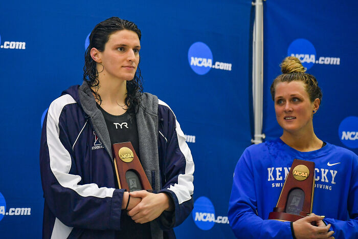 Two female swimmers holding NCAA trophies at an award ceremony, related to AOC&rsquo;s viral tweet clapping back.