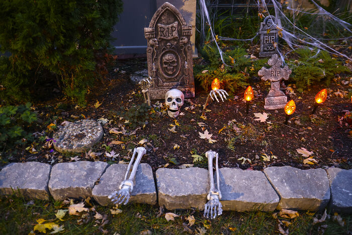 Halloween decorations with tombstones, skeleton parts, and glowing orange lights in a yard setting for seasonal display.
