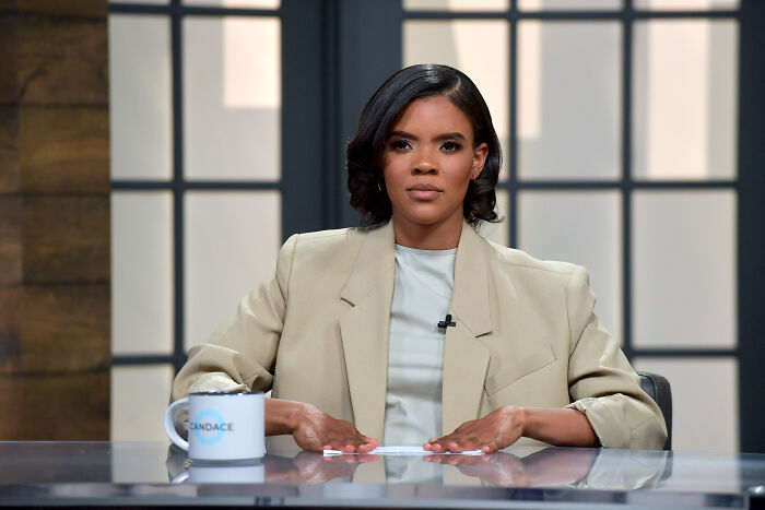 Candace Owens seated at a desk in a beige blazer, speaking about the Charlie Kirk gag order case.