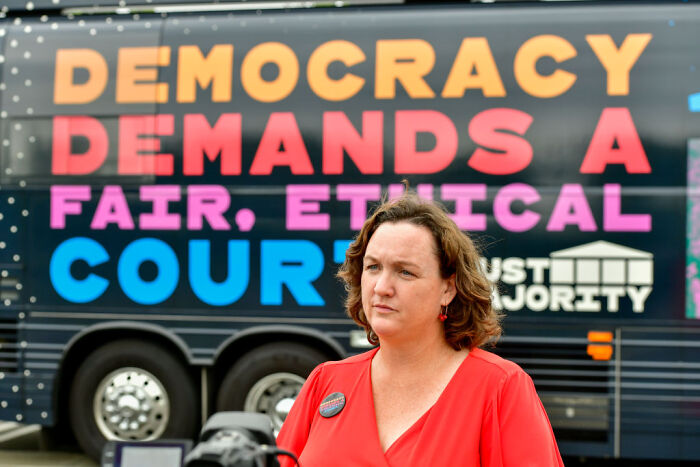 Katie Porter standing in front of a bus with democracy demands text, California governor hopeful engaged in campaign event.