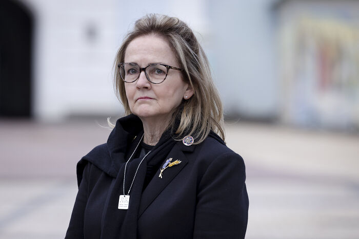 Woman wearing glasses and a black coat outdoors, appearing serious, related to House Speaker Mike Johnson and Trump unhinged topic.