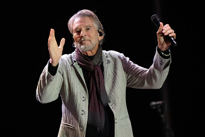 Singer of Danger Zone performing on stage, holding a microphone and gesturing with his hand during a live concert.