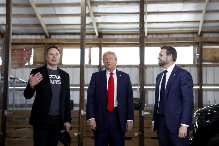 Three men standing inside a wooden barn, discussing a mysterious red cap figure linked to ancient Hopi prophecy.