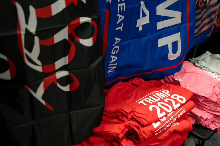 Trump 2028 shirts and flags stacked on a table, suggesting his presidency will continue indefinitely.