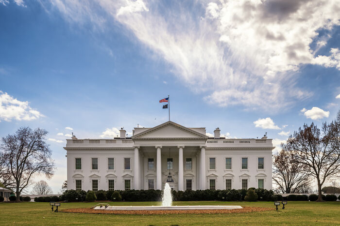 The White House with a fountain in front under a partly cloudy sky related to Trump supporter visa threat news.