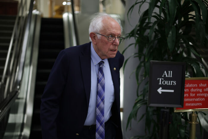 Maine Senate candidate walking near escalator, wearing glasses and suit, avoiding visible tattoo linked to hate symbol.