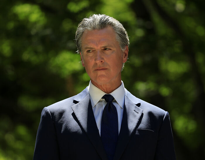 Gavin Newsom outdoors in a suit and tie, reacting to remarks about fat troops in a political context.