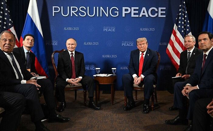 Donald Trump and Vladimir Putin seated during Alaska 2025 peace talks, amidst rising tensions and nuclear displays.