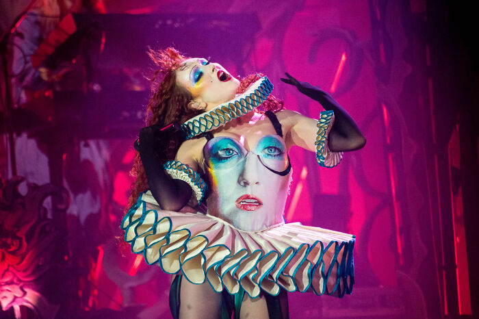 Chappell Roan performing on stage in a dramatic costume amid a vibrant, colorful theatrical lighting setting.