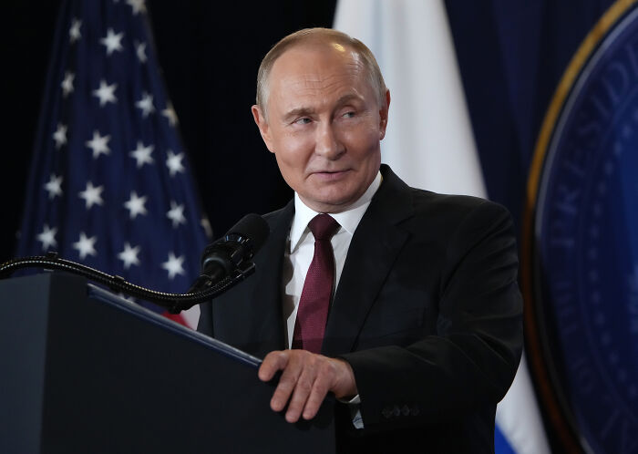 Vladimir Putin speaking at a podium with American and Russian flags, Russian leader flexes his nukes.