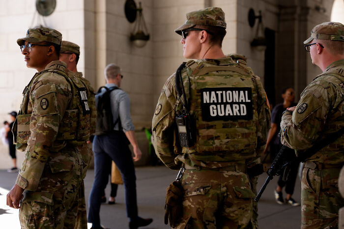 National Guard troops in camouflage uniforms stand alert in a public space, part of Chicago deployment efforts.