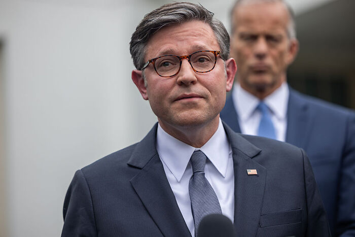 Man in a suit and glasses speaking at a press event as government shutdown debate intensifies between Dems and GOP leaders.