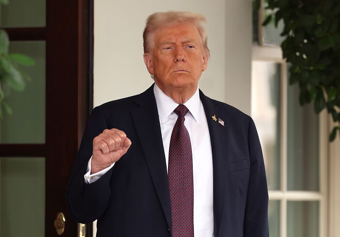 Donald Trump in a dark suit and tie, standing outside, with a raised fist gesture during a public appearance.