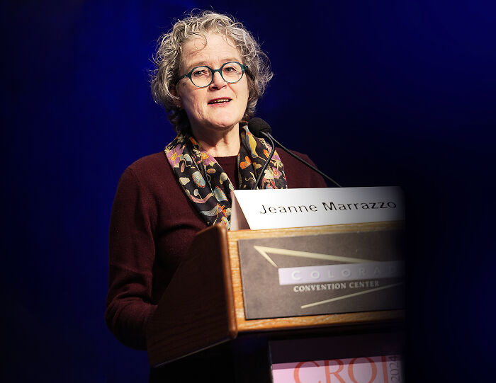 Woman with glasses speaking at a podium during an event related to infectious disease officials and whistleblower issues.