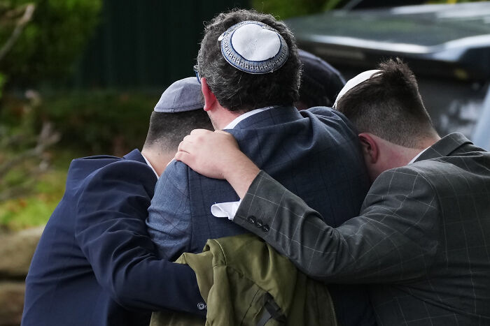 Three men wearing kippahs embracing each other outside a Manchester synagogue after terror attack on Yom Kippur.