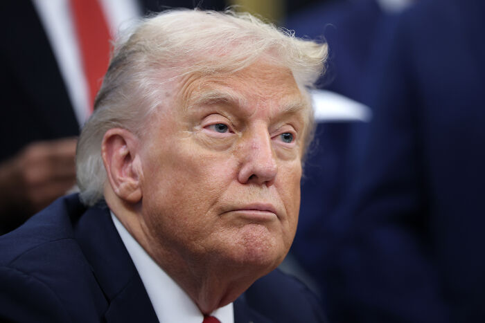 Donald Trump in a formal setting, attentively listening during a discussion about AI Medbed and transparency issues.