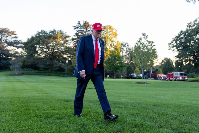 Man wearing a red cap and dark suit walking on grass, linked to ancient Hopi prophecy about a mysterious red cap figure.