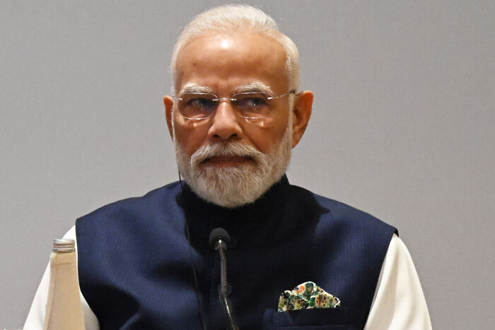 Prime Minister Narendra Modi seated wearing glasses and a navy vest at Asia Summit event with serious expression.
