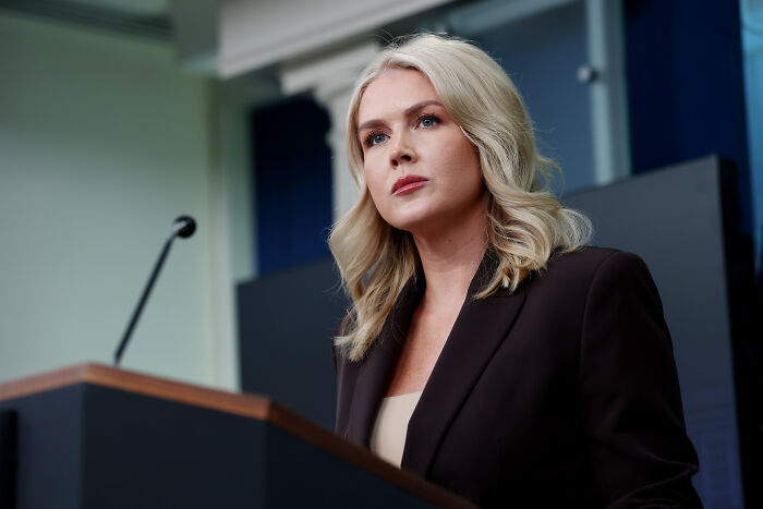 Karoline Leavitt speaking at a podium during a press event, discussing a bizarre text clash with a journalist.