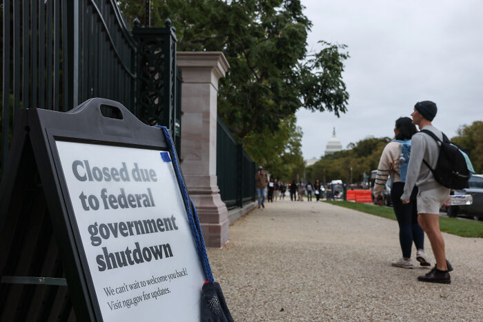 Sign about federal government shutdown outside Capitol, with pedestrians walking nearby, relating to Bernie Sanders and Trump trolling campaign.