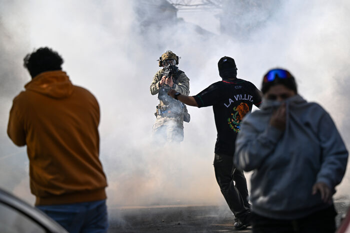 Protester faces armed officer in smoke-filled street during tense scene linked to ICE raids in Chicago.