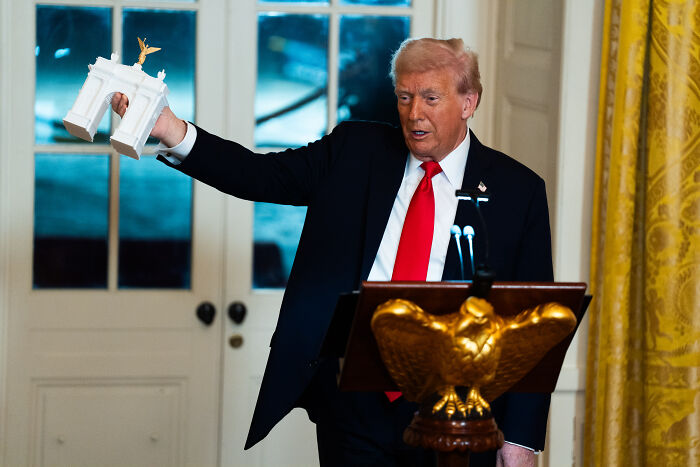 Donald Trump holding a white decorative model in the White House, highlighting design disasters in costly renovation project.