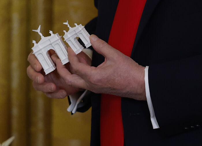Close-up of hands holding small white architectural models representing D.C. renovations tied to Trump&rsquo;s controversial oversight changes.