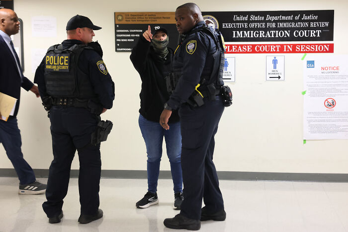 Two police officers in uniforms speaking with a person inside an immigration court, related to mistaken deportation after ICE error.