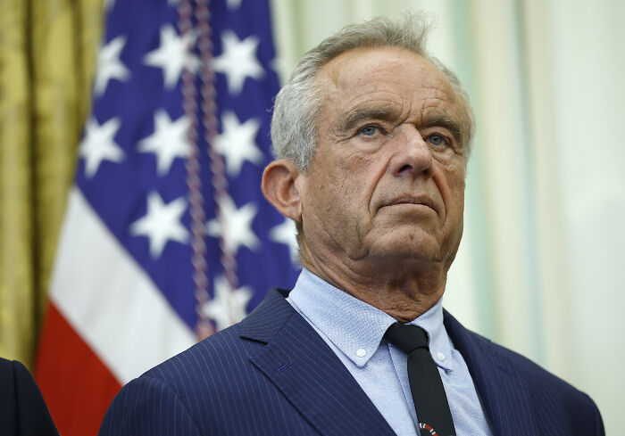 Man in a navy suit and tie standing in front of an American flag, symbolizing government focus during shutdown