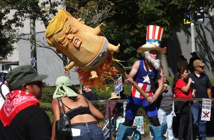 Protester in a patriotic costume holding a large effigy of Donald Trump at a public demonstration event.