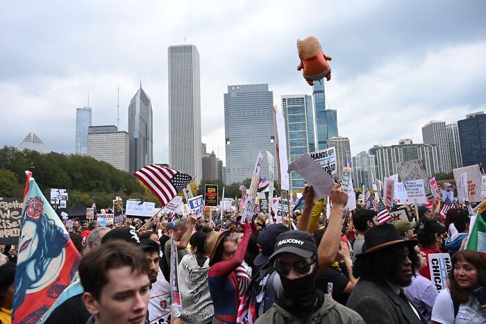 Crowd at No Kings protest in Chicago with signs and flags, highlighting viral elementary school teacher mocking Charlie Kirk.