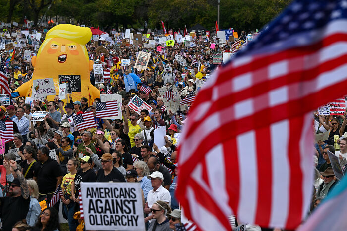 Crowd at a protest with American flags and signs showing Americans against oligarchy during government shutdown focus.