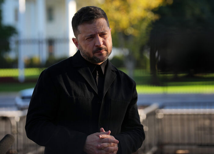 A man in a black coat speaking outdoors with a serious expression, news related to Russian leader flexing nukes.
