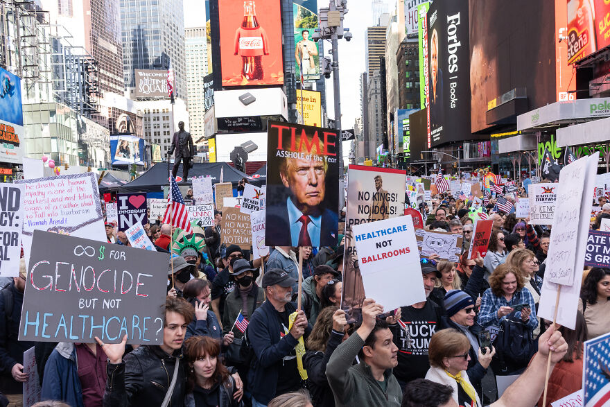 Crowd holding protest signs including doctored photo of Trump and JD Vance, highlighting White House shared manipulated royal image.