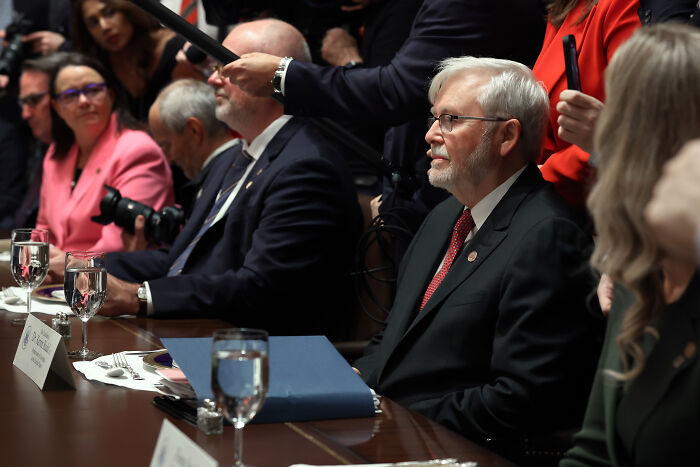 Man in glasses and suit sitting at a table during a White House meeting amid Trump visitor controversy over nuts remark.
