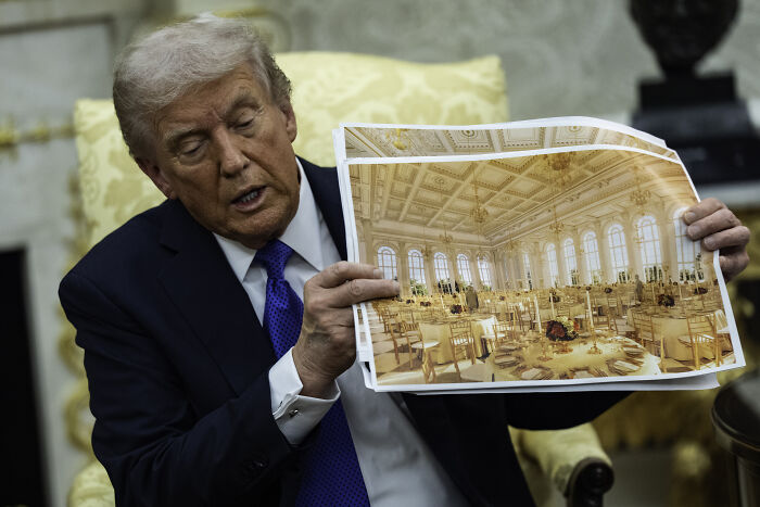 Donald Trump holding a large photo of a banquet hall showing design disasters in costly White House renovation project.