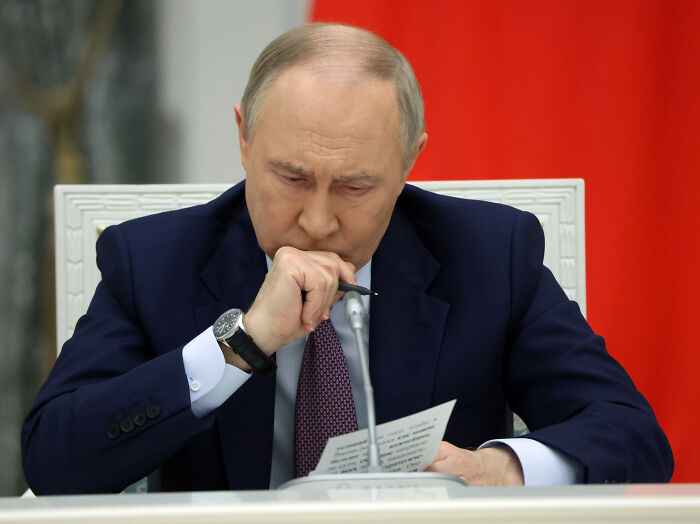A man in a dark suit studying a document with a pen, symbolizing nuclear weapons testing and Pentagon orders.