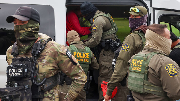 Border Patrol police in tactical gear escort detainees into a van during an ICE operation involving mistaken deportation.