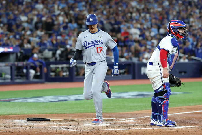 Los Angeles Dodgers player rounding the bases during the World Series game with catcher in full gear behind home plate.