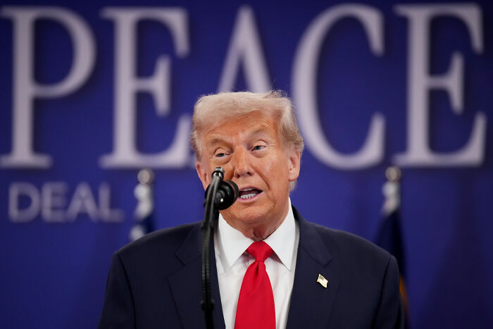 Donald Trump speaking at a podium with a microphone, in a dark suit and red tie at an Asia Summit event.
