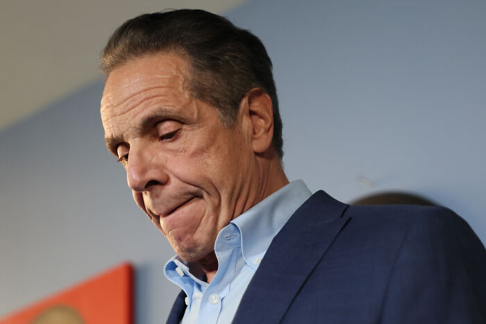 Man in a blue suit looking down thoughtfully, representing NYC mayoral frontrunner Zohran Mamdani facing criminal referrals.