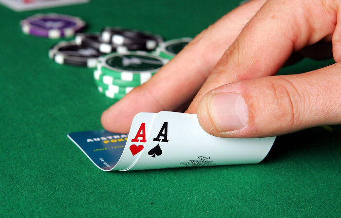 Hand holding two aces on a poker table with chips nearby, illustrating NBA gambling cases involving insider bets and rigged games.