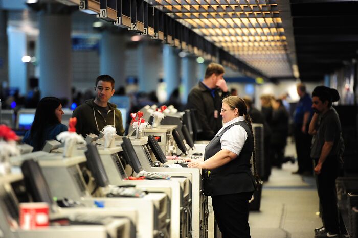 Airport check-in counters with staff assisting passengers in a busy terminal, highlighting airports and government shutdown context.